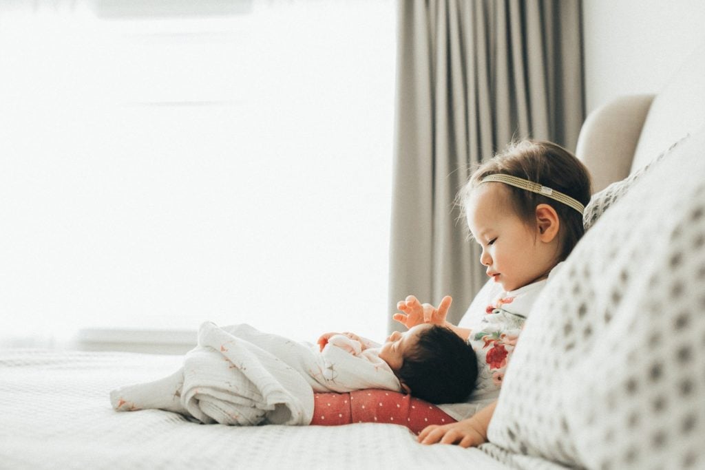 toddler holding newborn sister on bed montreal family photographer