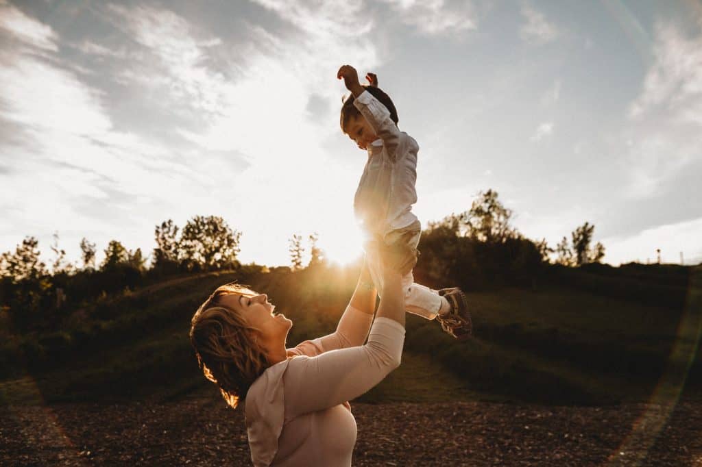 Mother and son outside at sunset, swinging little boy in the air and laughing