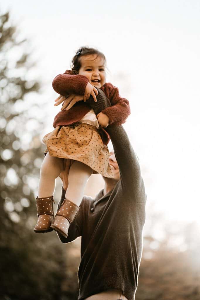 Dad swinging laughing daughter in the air in autumn at Beaver Lake park