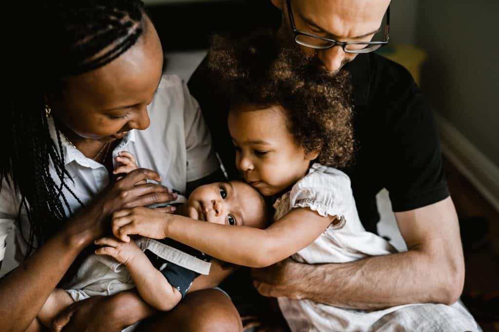 family cuddling with toddler kissing baby brother