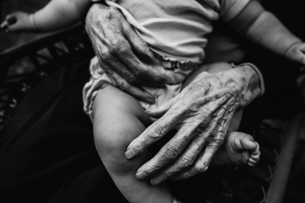 Close up of great grandmother's hands holding little baby