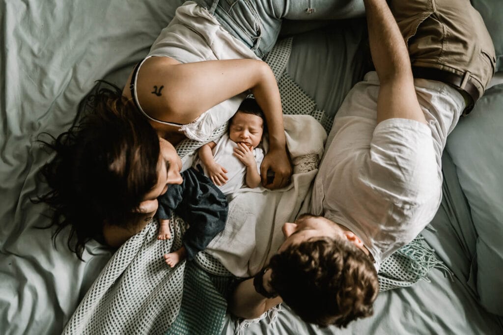 new mom and dad lying on bed with newborn baby