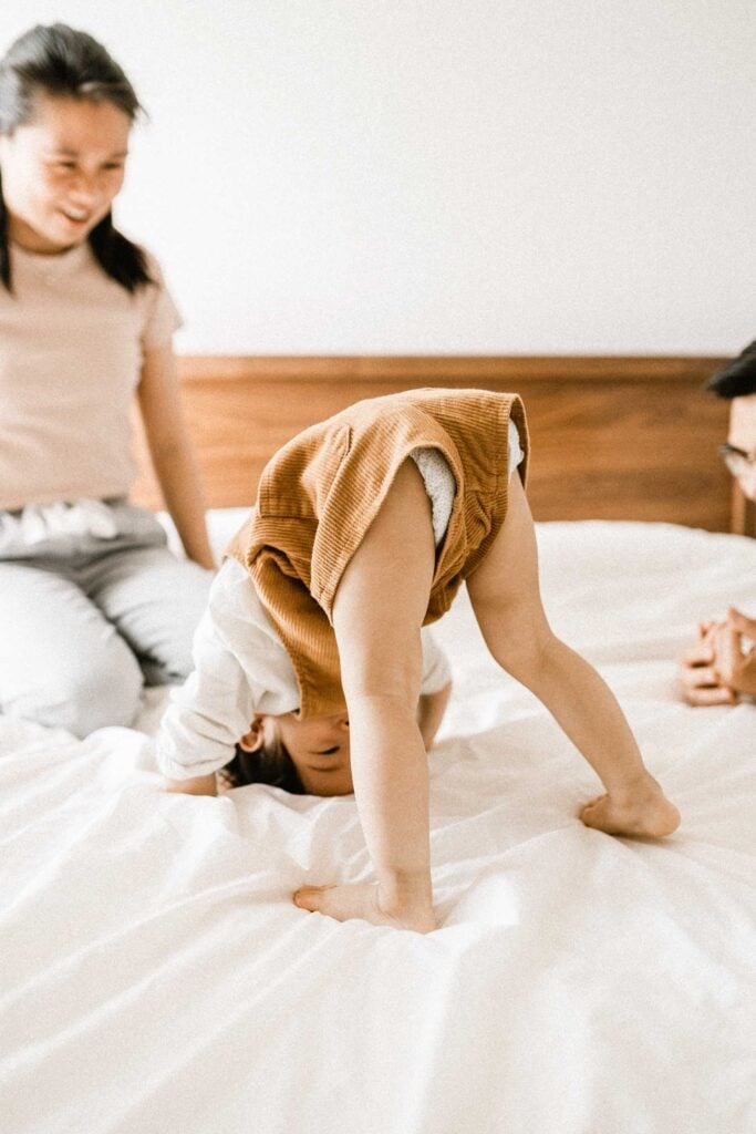 child trying to do handstand on bed as mom watches