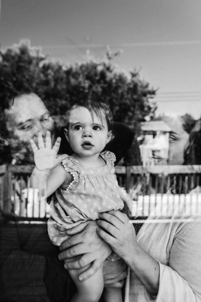 mom and dad holding baby reflected through the window
