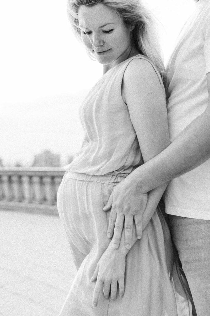 black and white image of pregnant woman leaning on her partners chest