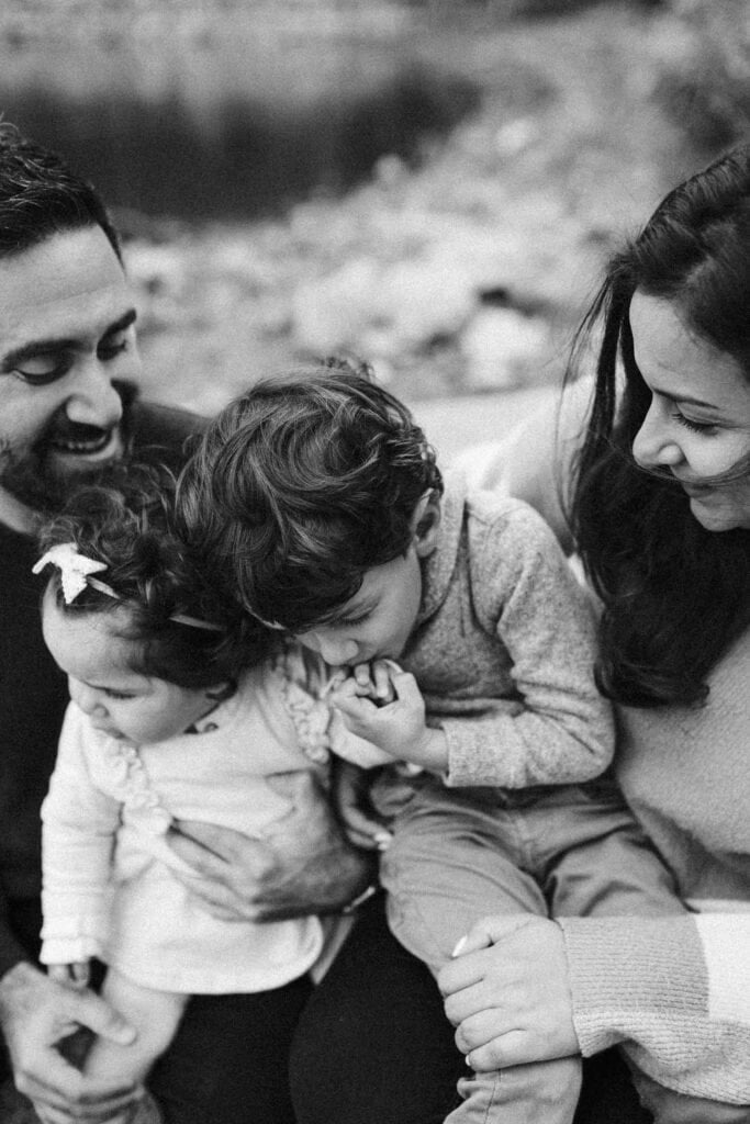 little boy kisses his sister's hand while sitting on parents laps