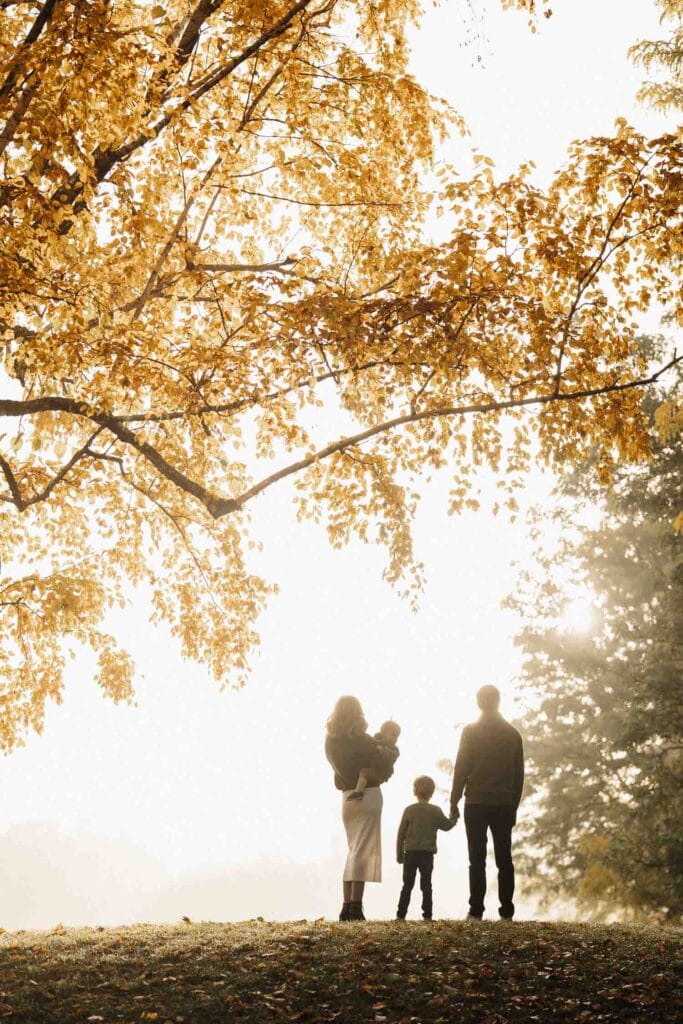 family stands under yellow autumn tree in park surrounded by fog