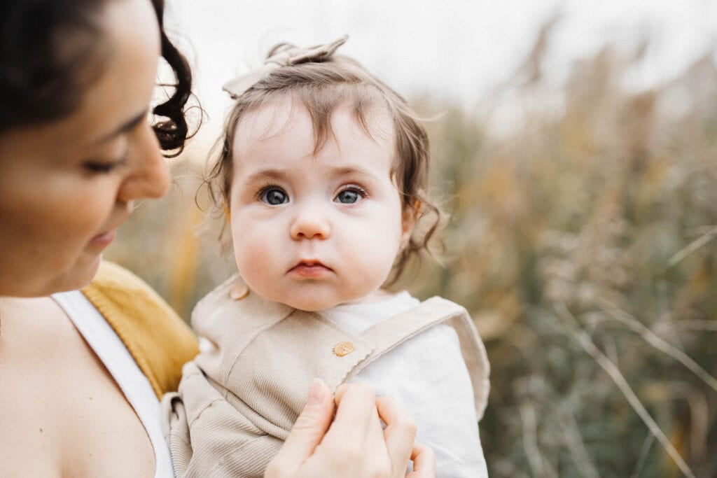 baby girl looking at camera as mom looks at her as they stand in a field in Laval