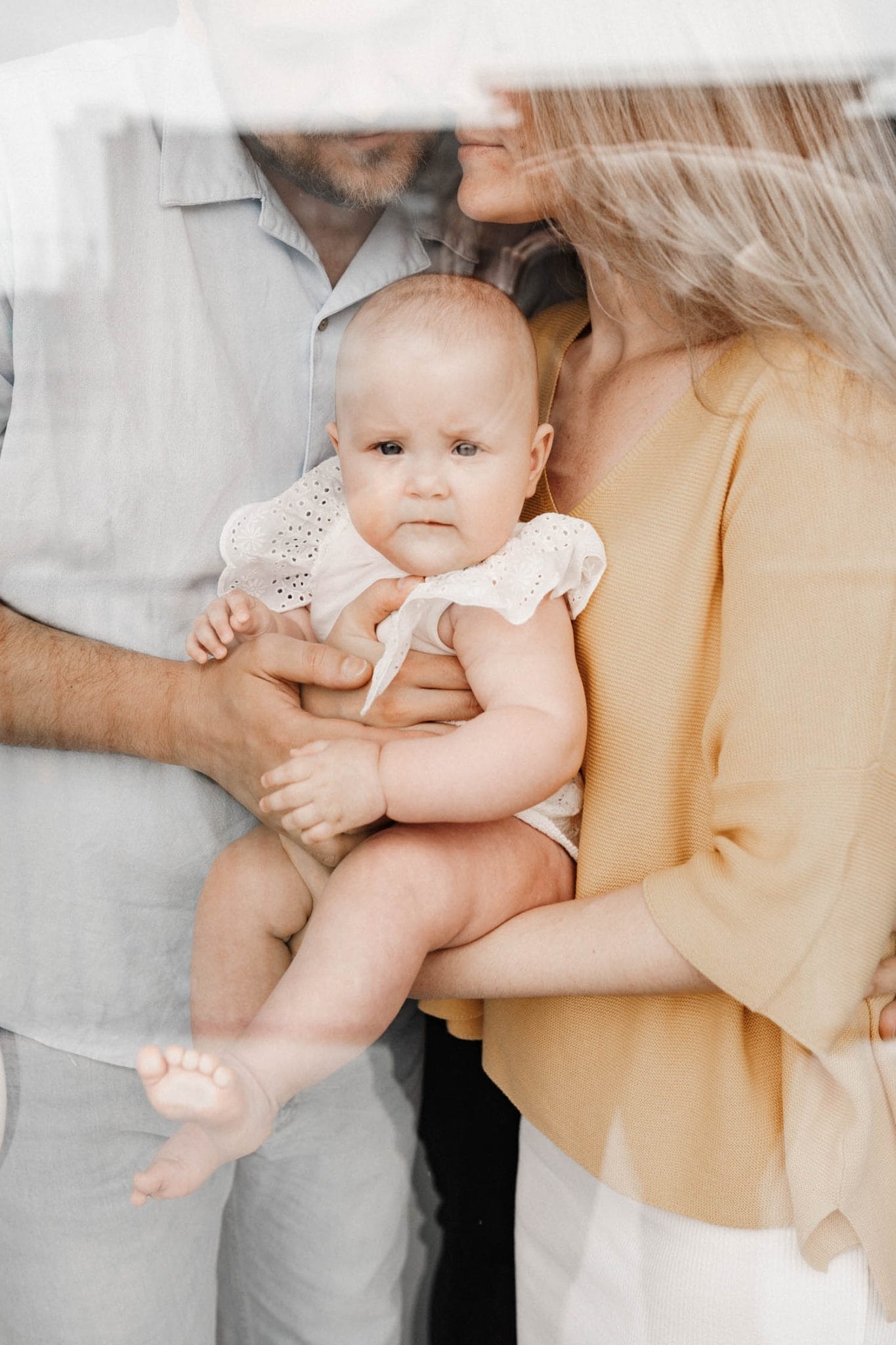 mom and dad hold baby as seen through glass doors