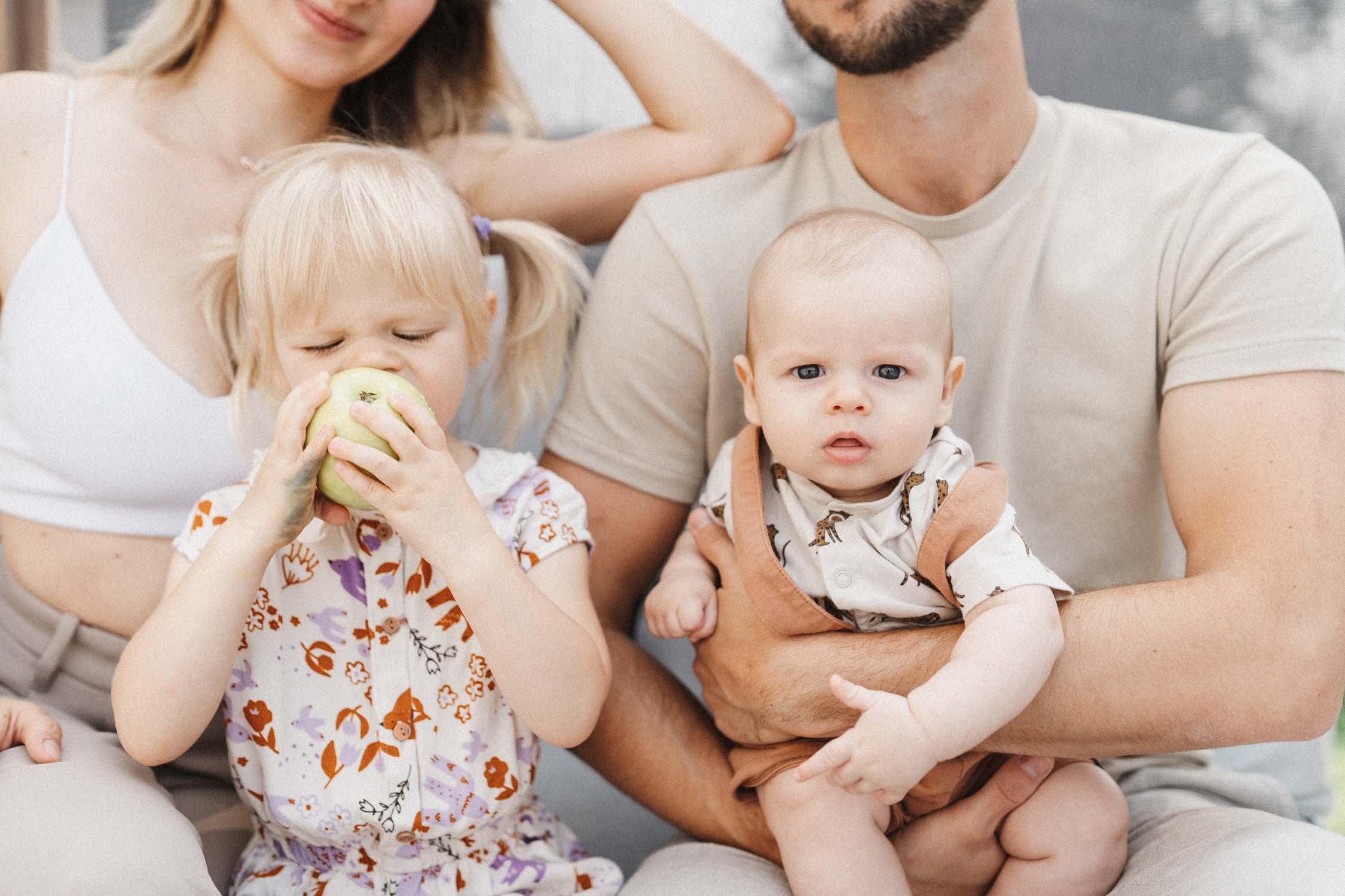 Siblings sitting on parents lap, while one eats an apple during their in-home family photo session in montreal