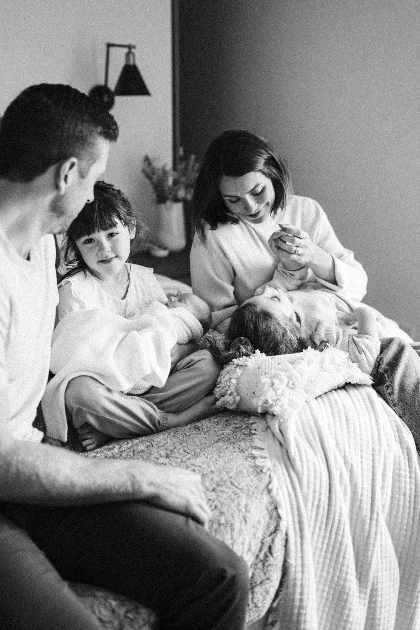 Family with 3 kids sits on bed during their family photo session at home in Montreal