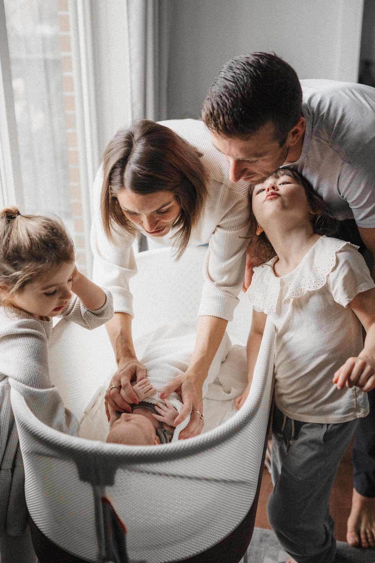 Family admiring newborn baby girl in her bassinet during in-home family photoshoot in Montreal.