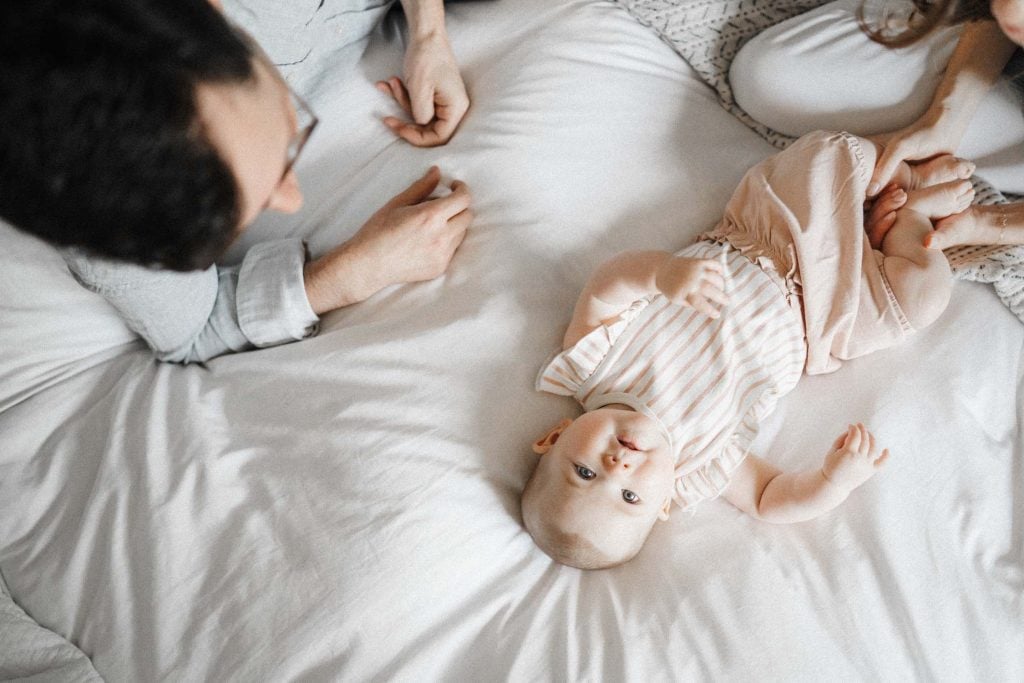 little baby laying on bed looking up as parents look over her