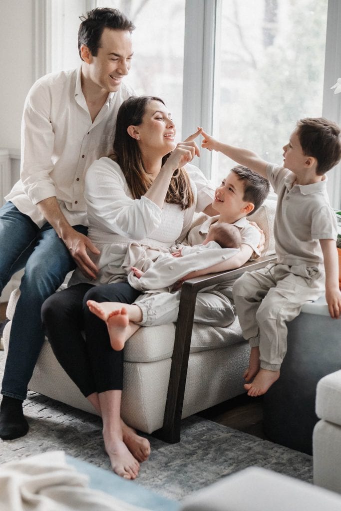 mom plays with her sons while holding newborn baby girl in her lap as dad looks over her shoulder