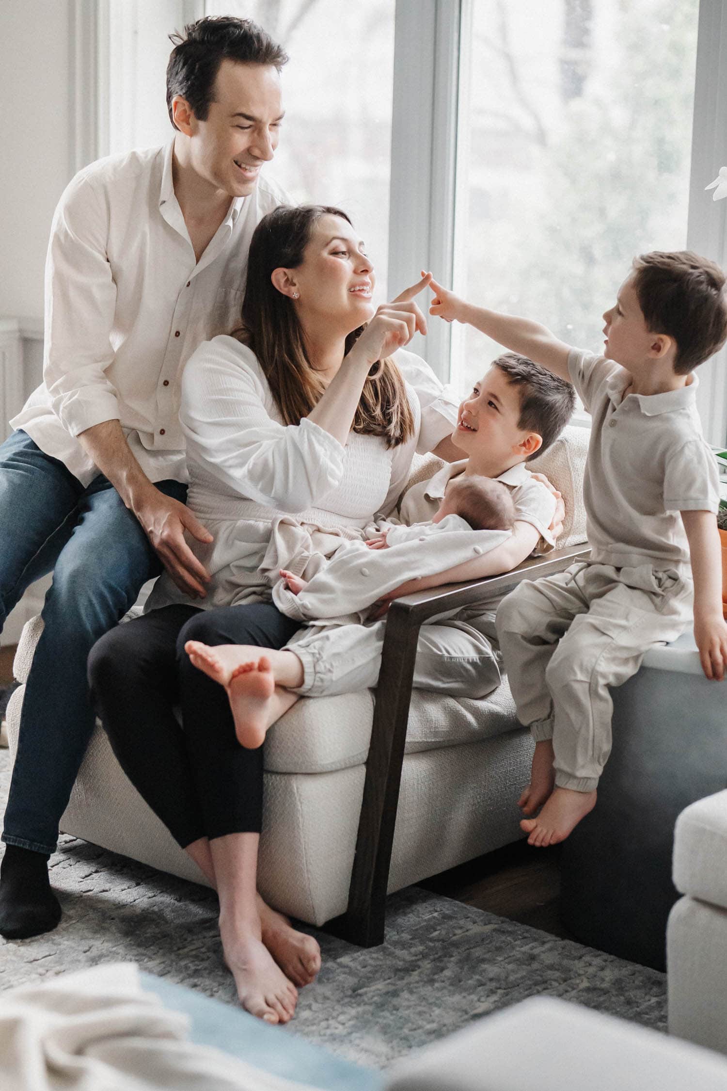 mom plays with her sons while holding newborn baby girl in her lap as dad looks over her shoulder