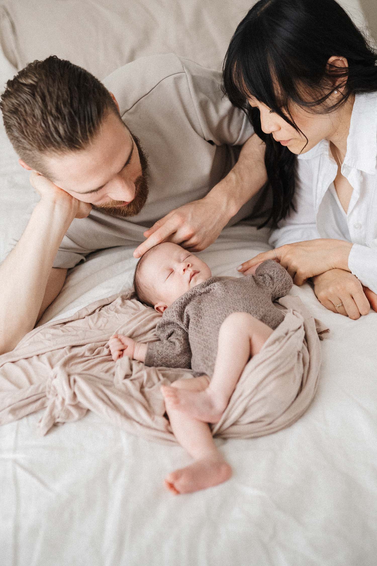 mom and dad look over newborn baby who is laying on the bed