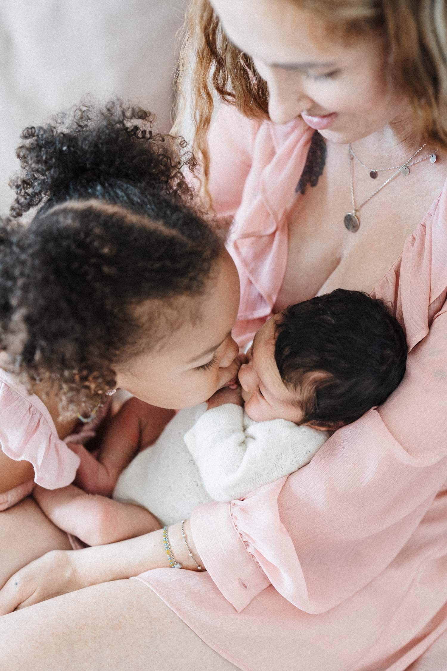 Toddler kisses her newborn sister during in-home family photo session