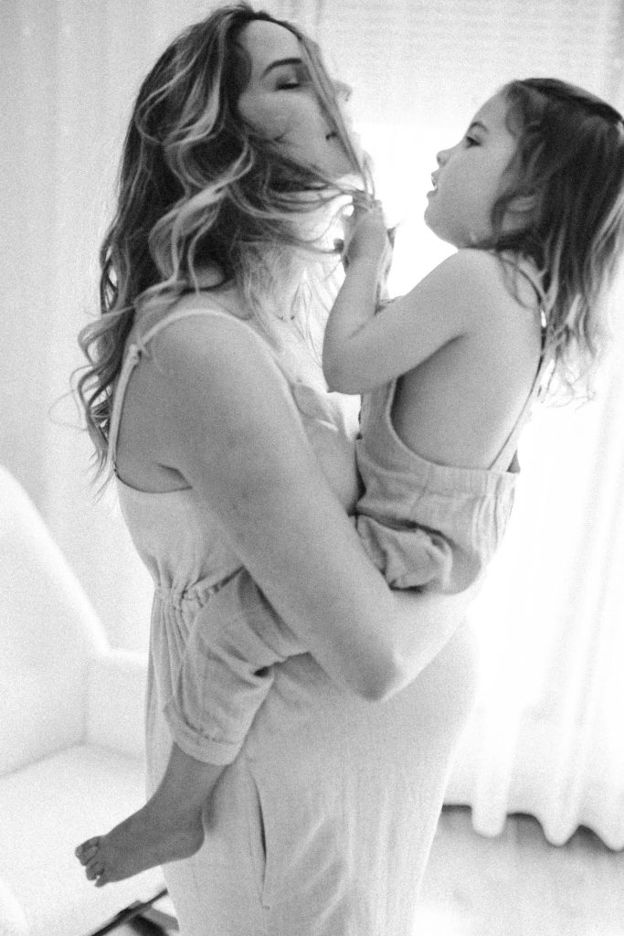 Little girl in pregnant mom's arms pulls mom's hair during their at home maternity photoshoot