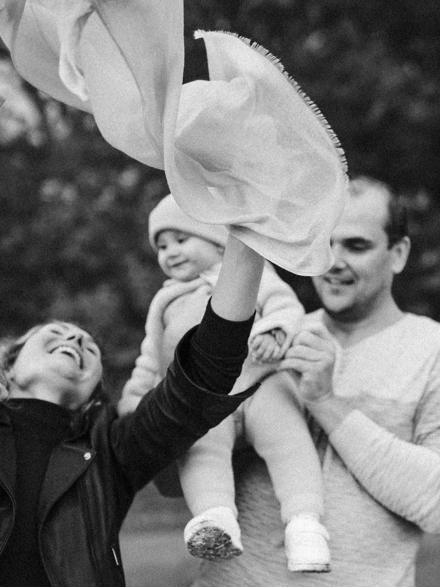 Mom laughs as she throws a scarf in the air as baby girl looks on smiling. montreal family photo session