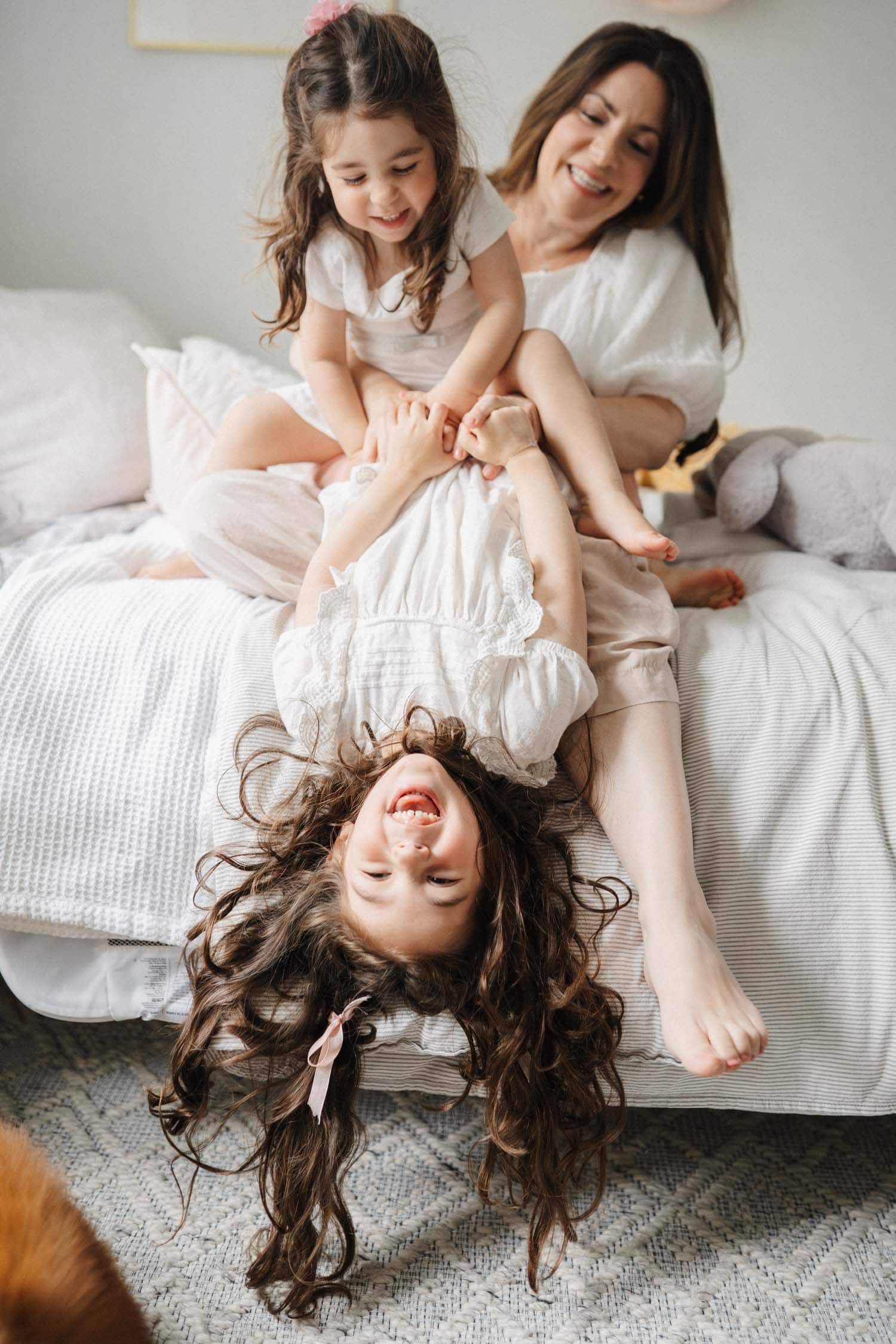 Little girl hangs off bed as mom and sister hold her up during their relaxed family photo session in Montreal