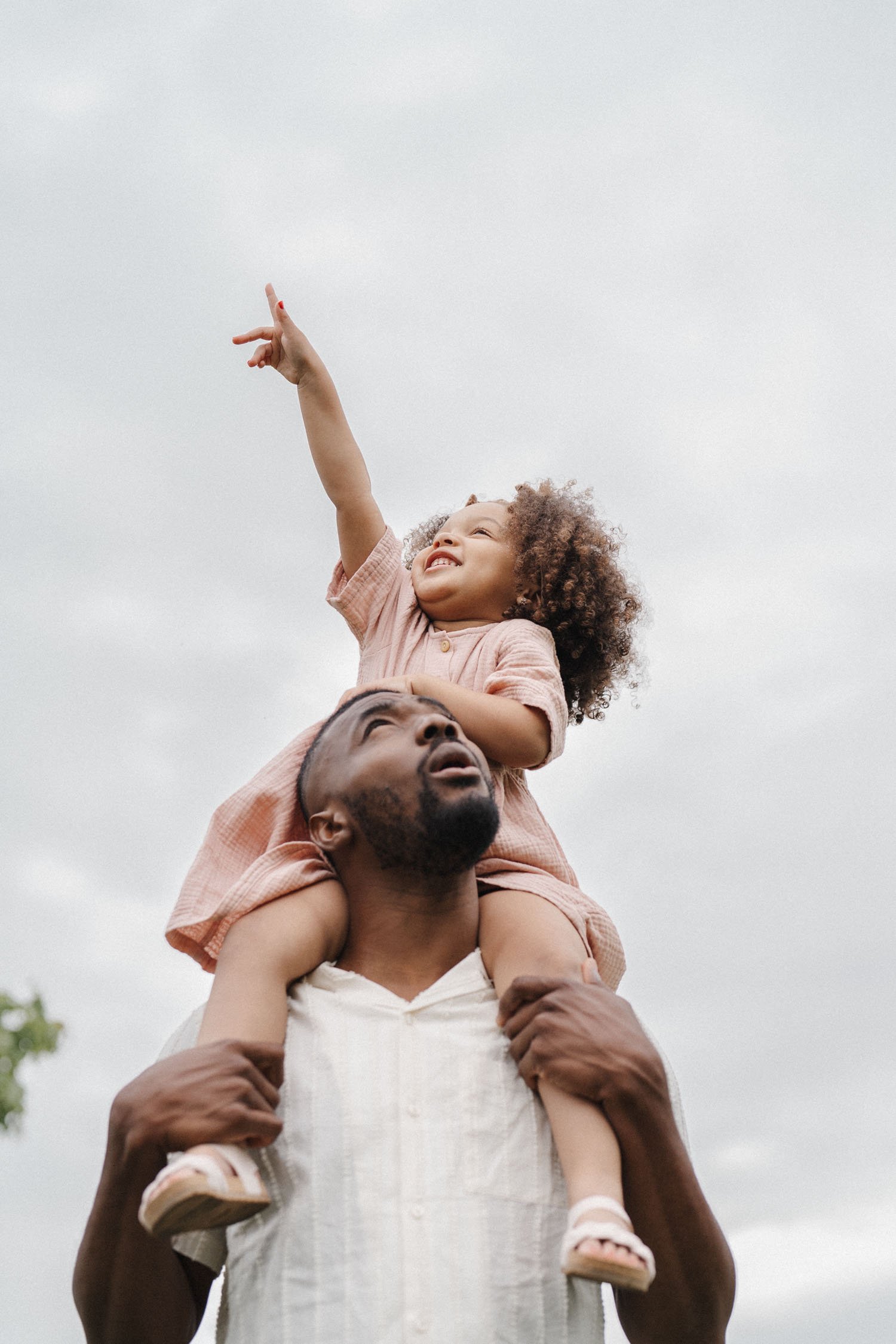Little girl sitting on her dad's shoulder while pointing up to the sky during their family photo session in Montreal