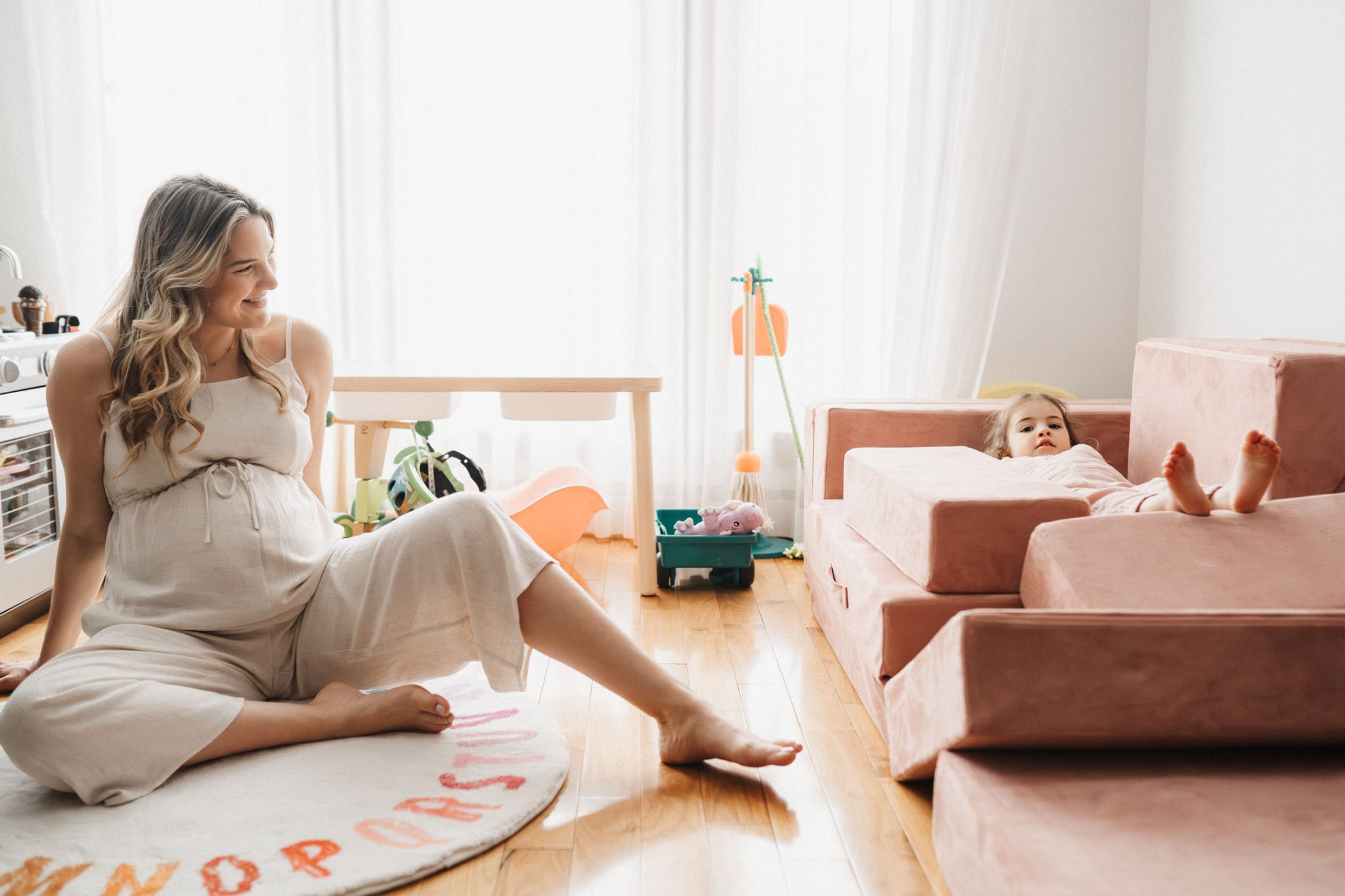 Pregnant woman sits on the floor while her toddler is silly next to her during their in-home montreal area photo shoot