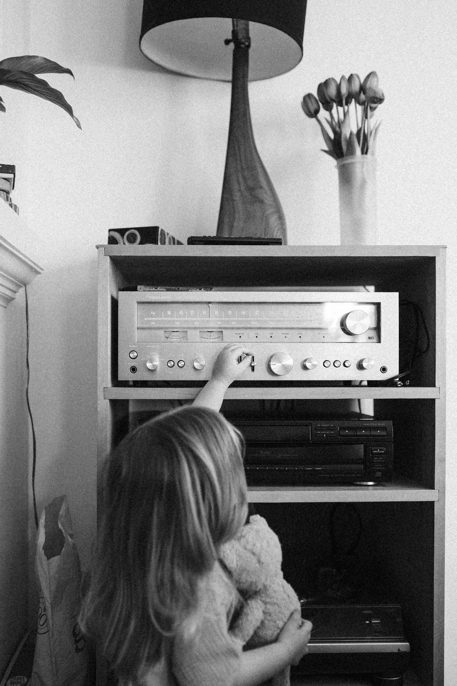 LIttle gifl holding a teddy bear adjusts the volume on their vintage stereo during their in-home family photoshoot in Montreal