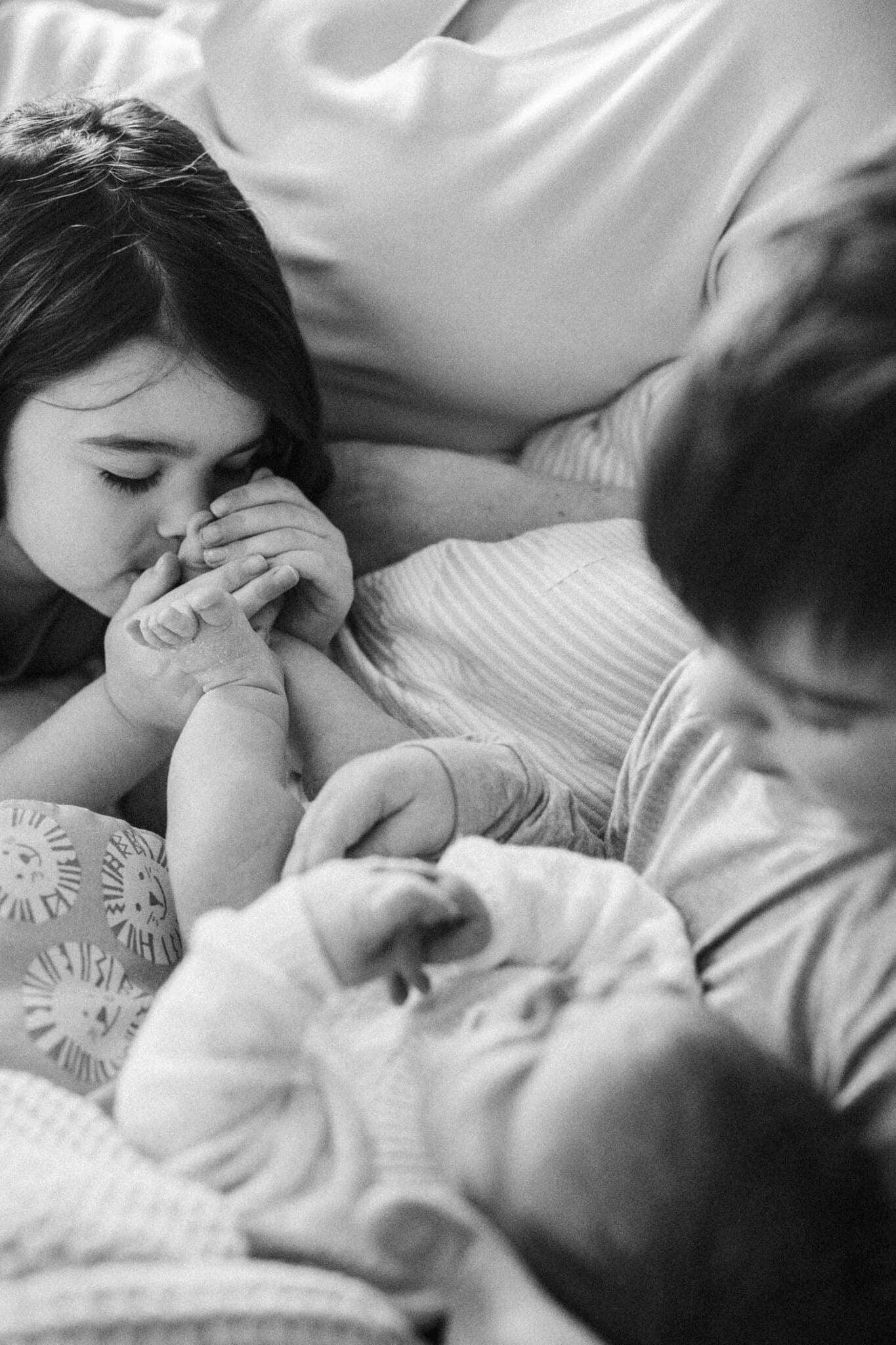 Big sister kisses her newborn sister's feet during their at-home newborn photo shoot in Montreal