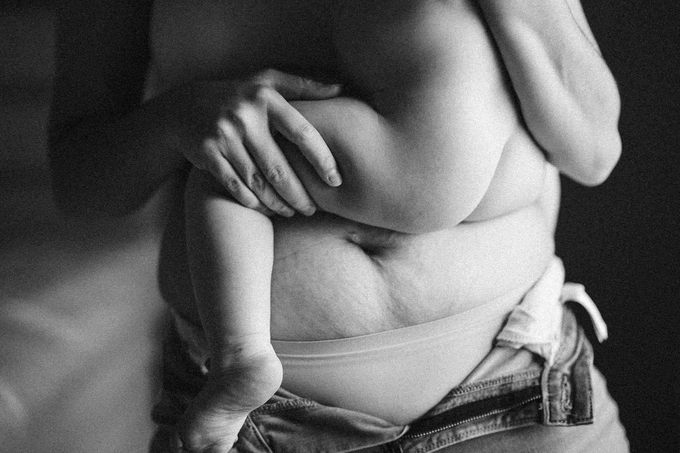 Mom shows her post pregnancy belly while holding her baby in her arms during their in-home family photo session