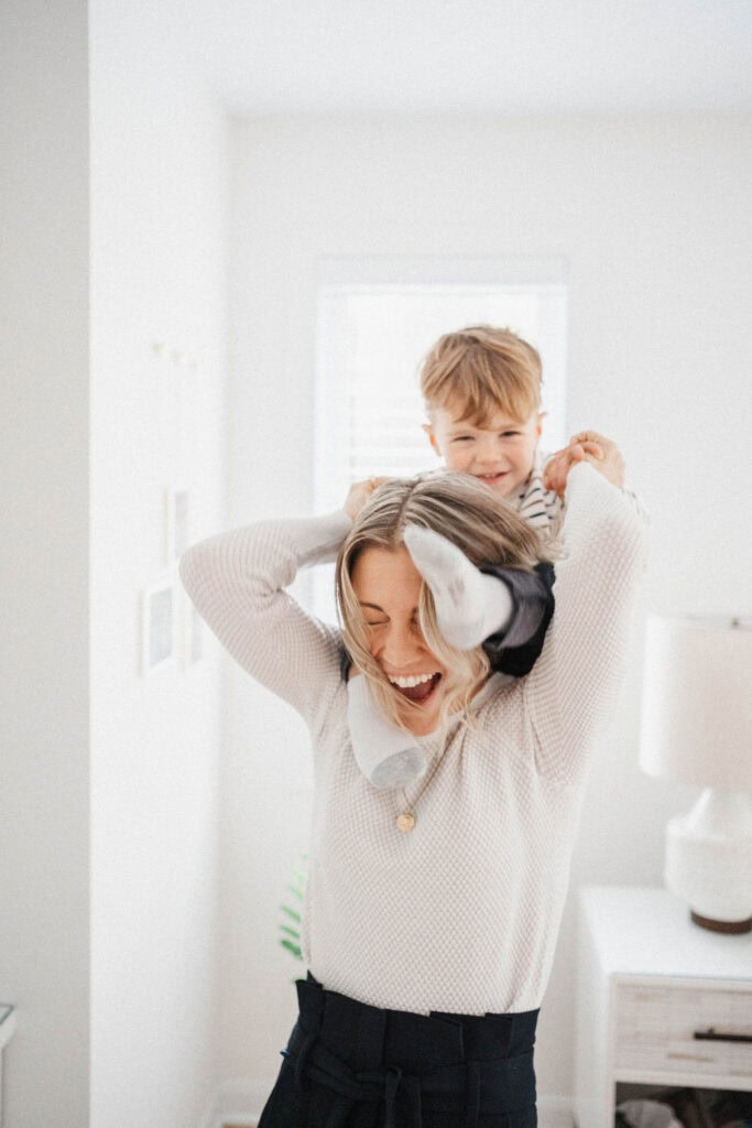 Mom laughs while toddler sits on her shoulders at home during their family photo shoot in Montreal