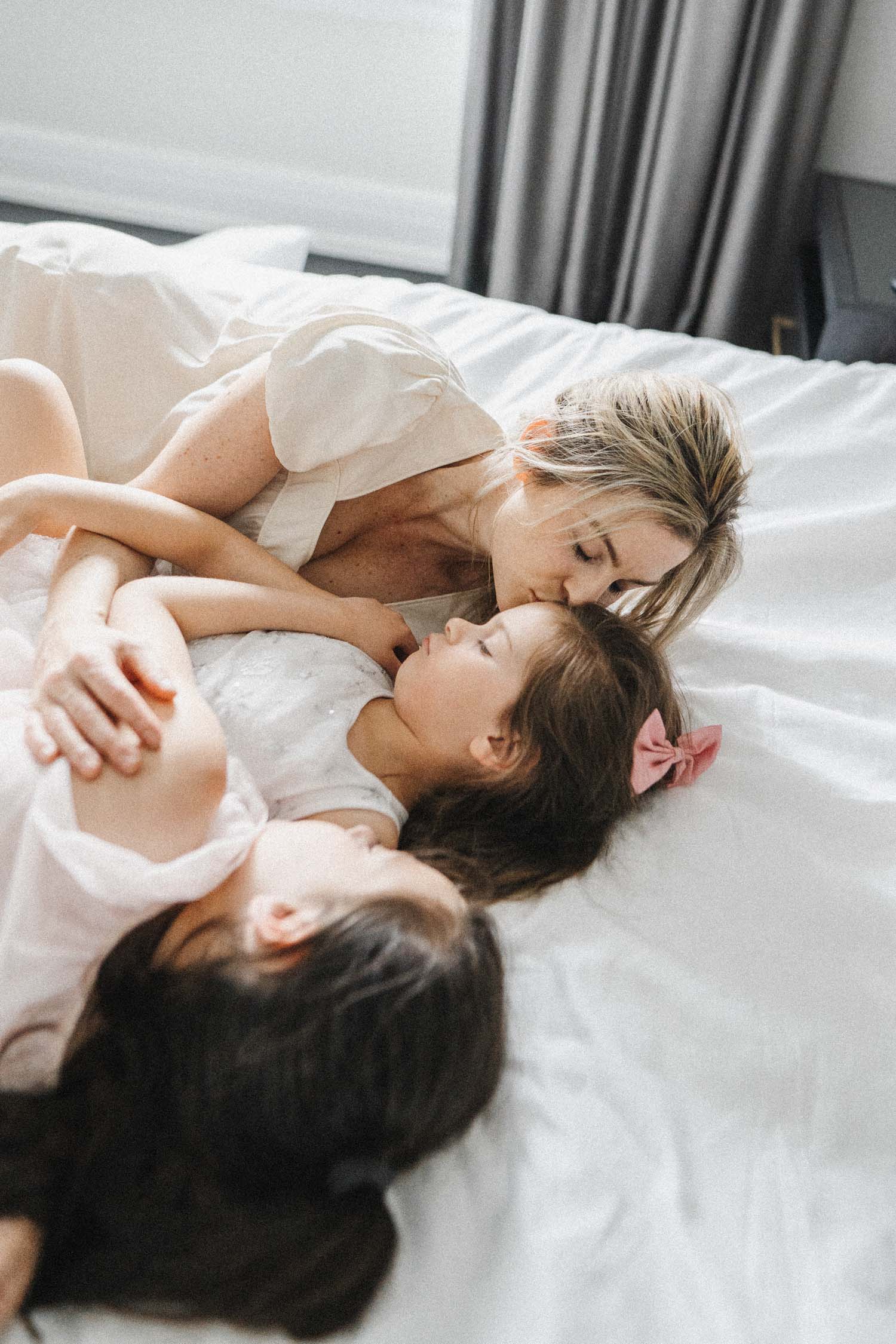 Mom kisses daughter's forehead on bed during their in-home family photo shoot in Montreal